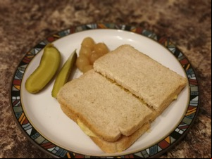 Halved brown crisp sandwich alongside pickles