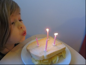 Child blowing out four candles on a crisp sandwich